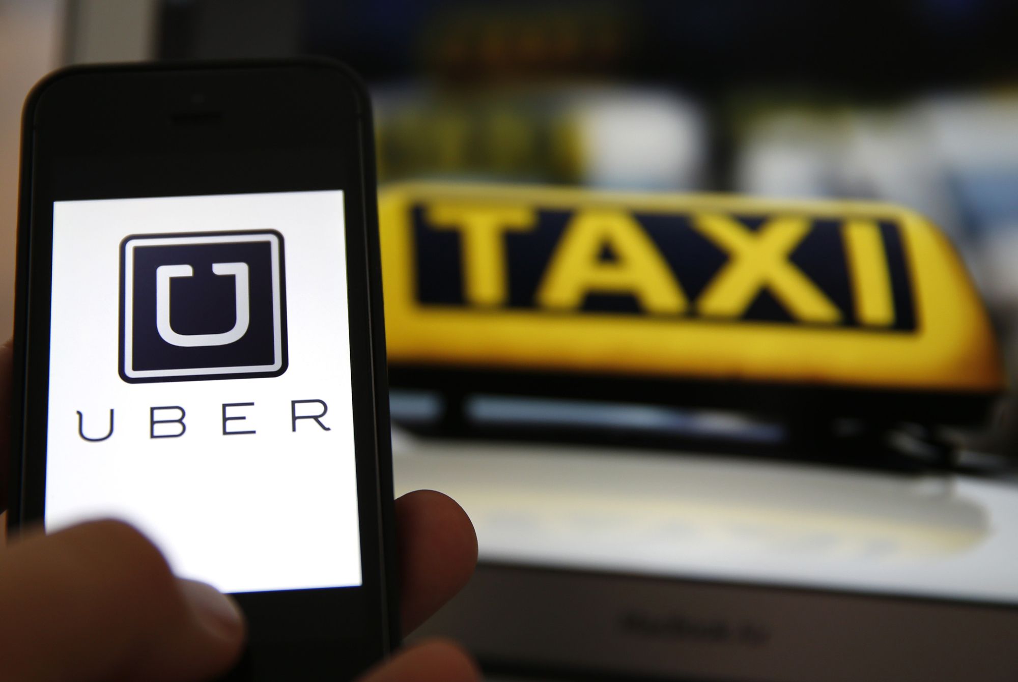 File illustration picture showing the logo of car sharing service app Uber on a smartphone next to the picture of an official German taxi sign