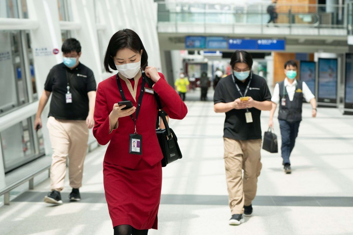 Un'hostess e due passeggeri all'aeroporto di Hong Kong in Cina, tutti con la mascherina