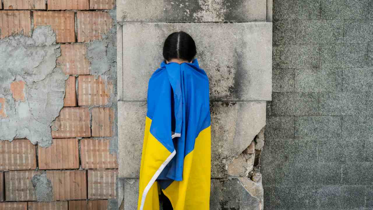 Bambina con bandiera ucraina davanti a un muro distrutto dalle bombe