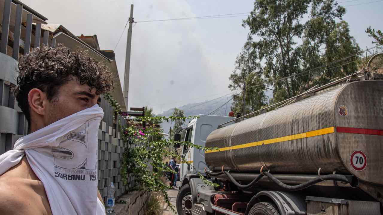 Palermo, un giovane si copre il volto durante gli incendi