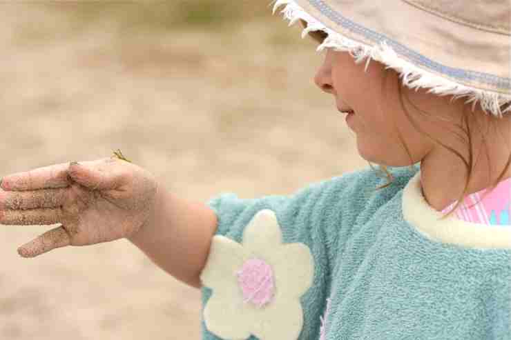 Bambina in spiaggia con cavalletta sulla mano